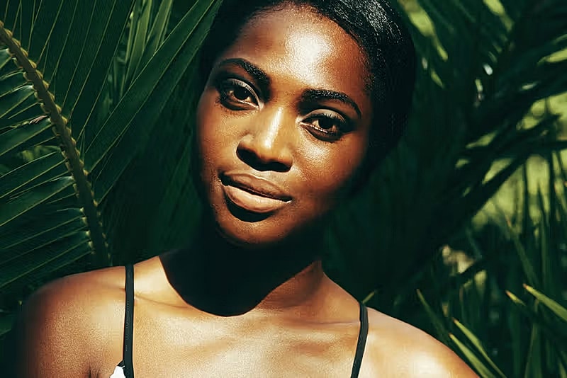 Woman posing confidently among green foliage.