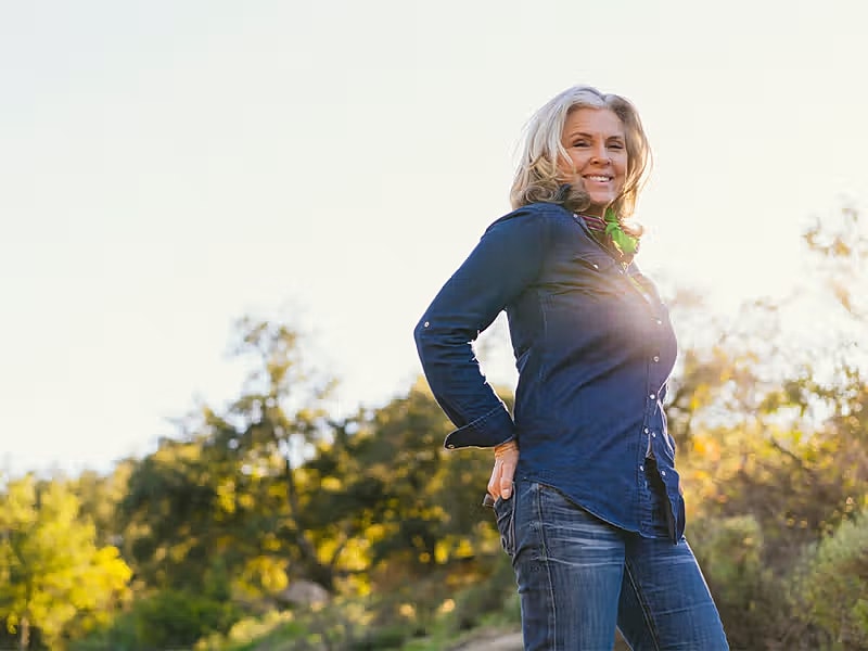 Smiling woman outdoors in sunlight, casual attire.