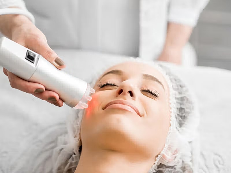 Woman receiving facial treatment with device.