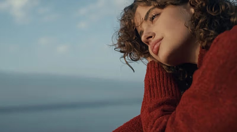 Woman in red sweater gazing at the ocean.